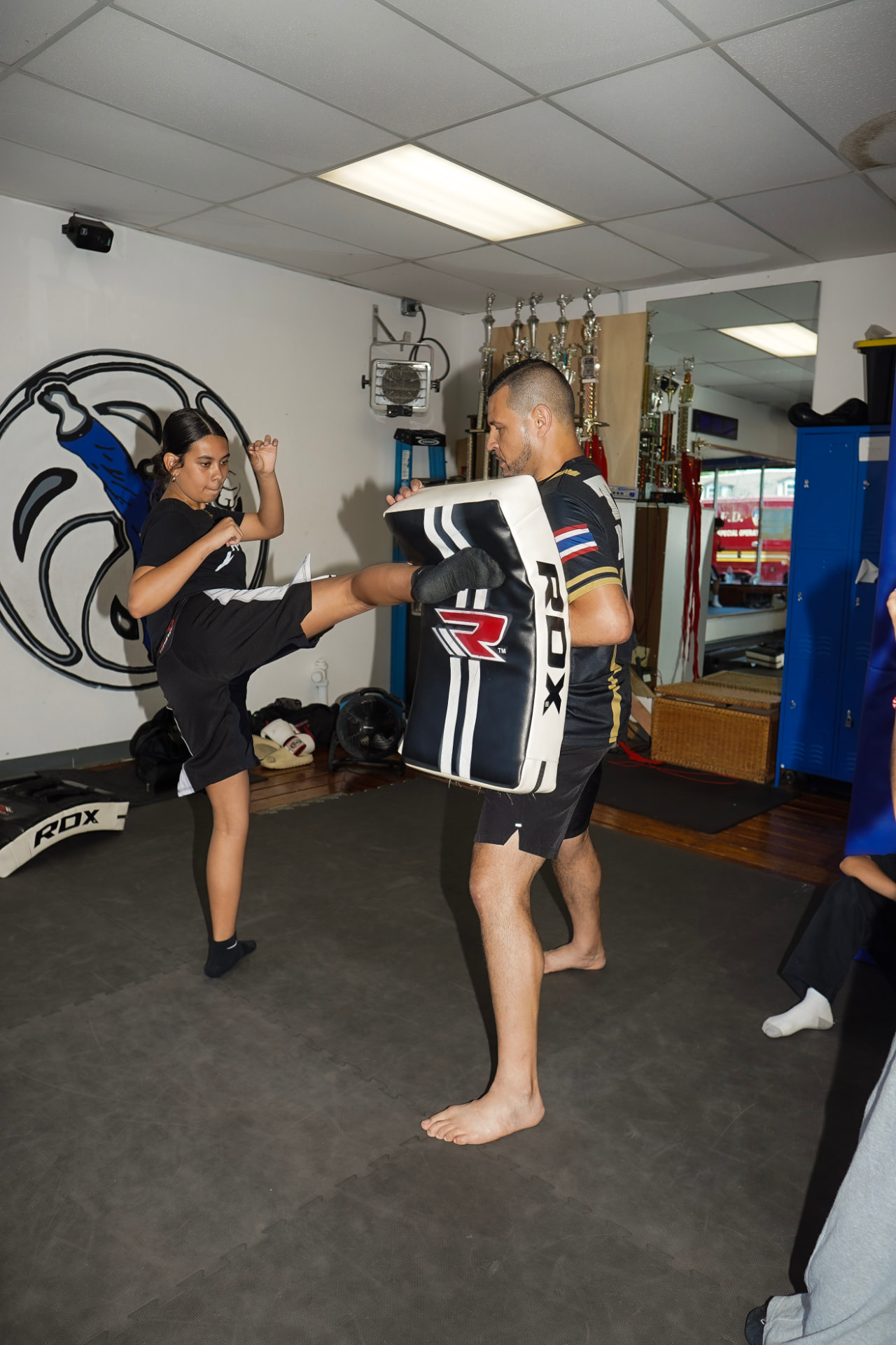 Student kicking a striking pad in front of the United Black Belt wall logo