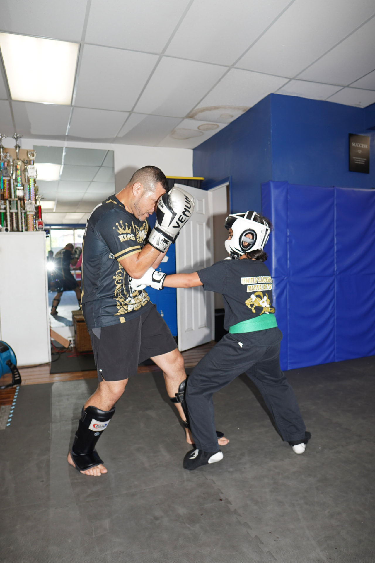Coach sparring with a young student wearing headgear and a green belt